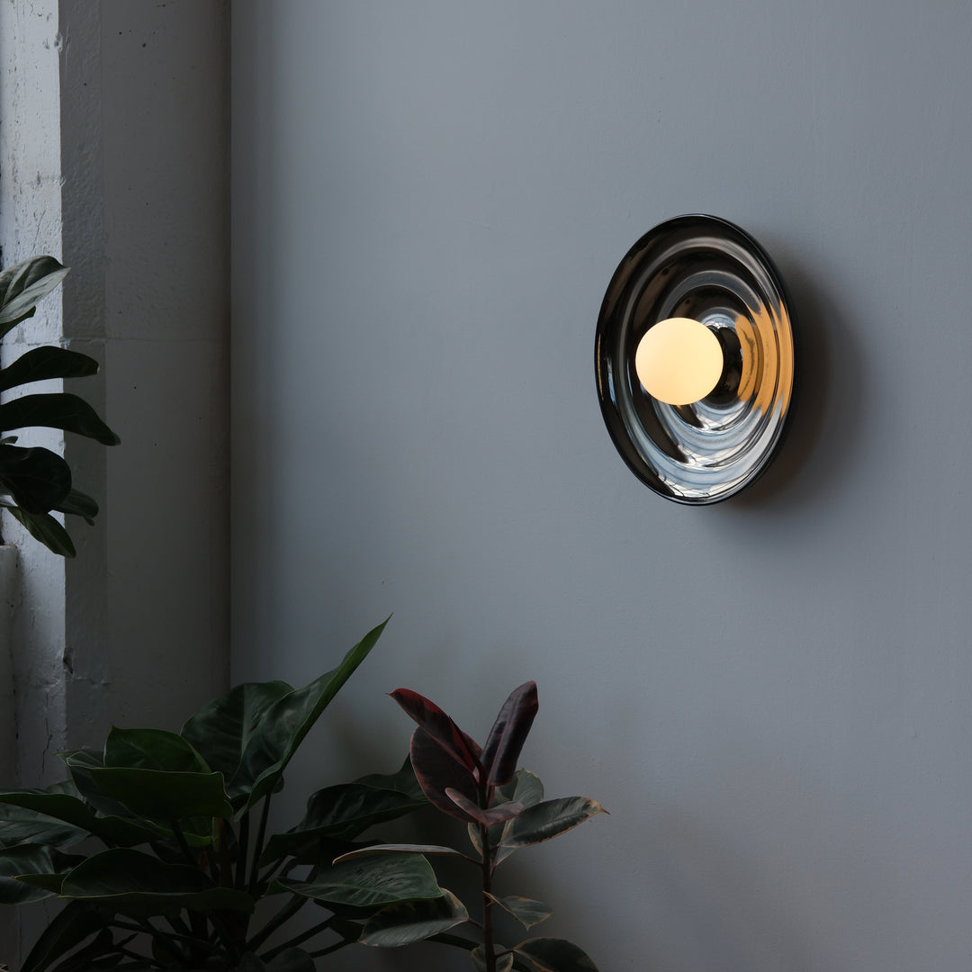 Sleek chrome wall sconce with warm glow, styled with lush greenery