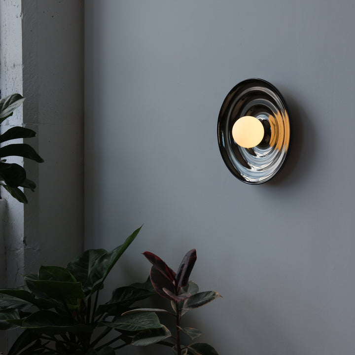 Sleek chrome wall sconce with warm glow, styled with lush greenery