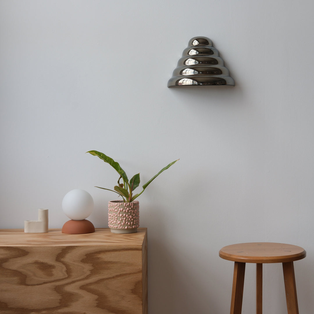 Layered metallic wall sconce above wooden console with textured planter and minimalist decor