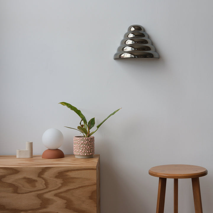 Layered metallic wall sconce above wooden console with textured planter and minimalist decor