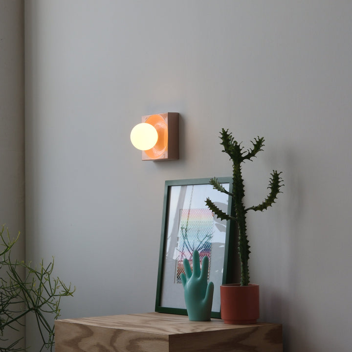Modern wall sconce with amber glass, styled with teal hand sculpture and potted cactus on oak console