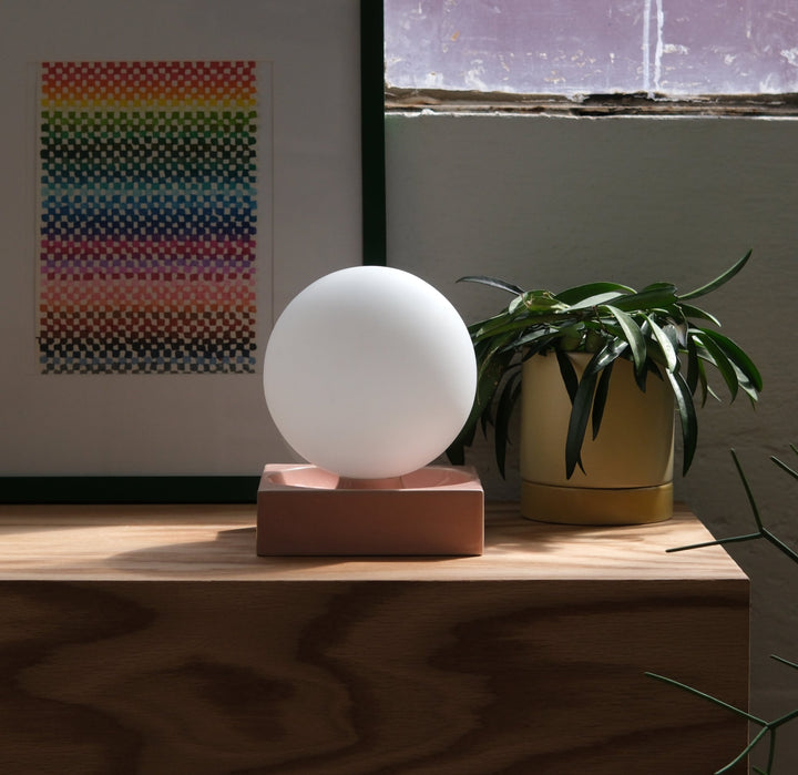 Frosted glass orb on blush ceramic base, styled with potted plant and rainbow art