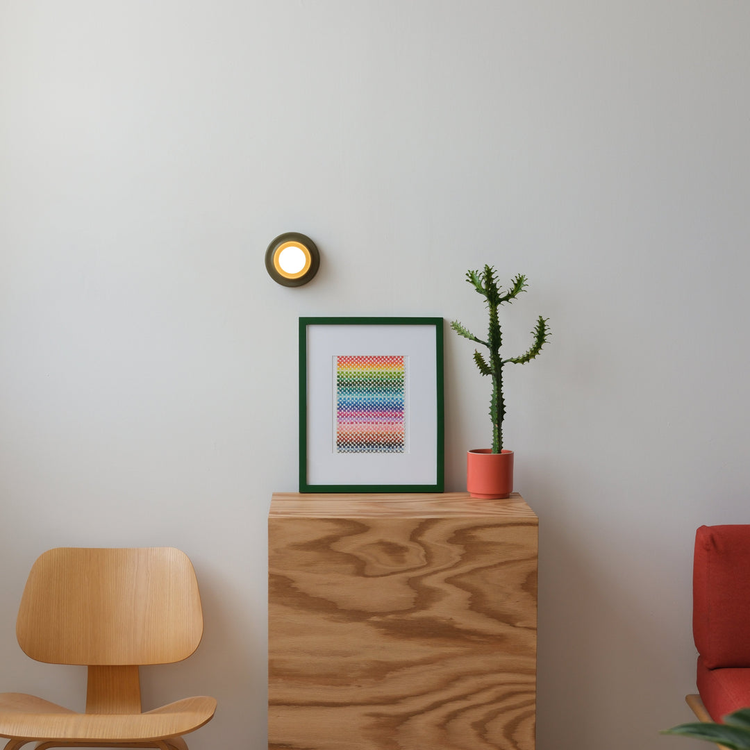 Eames-style oak chair beside a plywood console with framed rainbow art print, potted cactus, and wall sconce