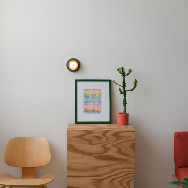 Eames-style oak chair beside a plywood console with framed rainbow art print, potted cactus, and wall sconce