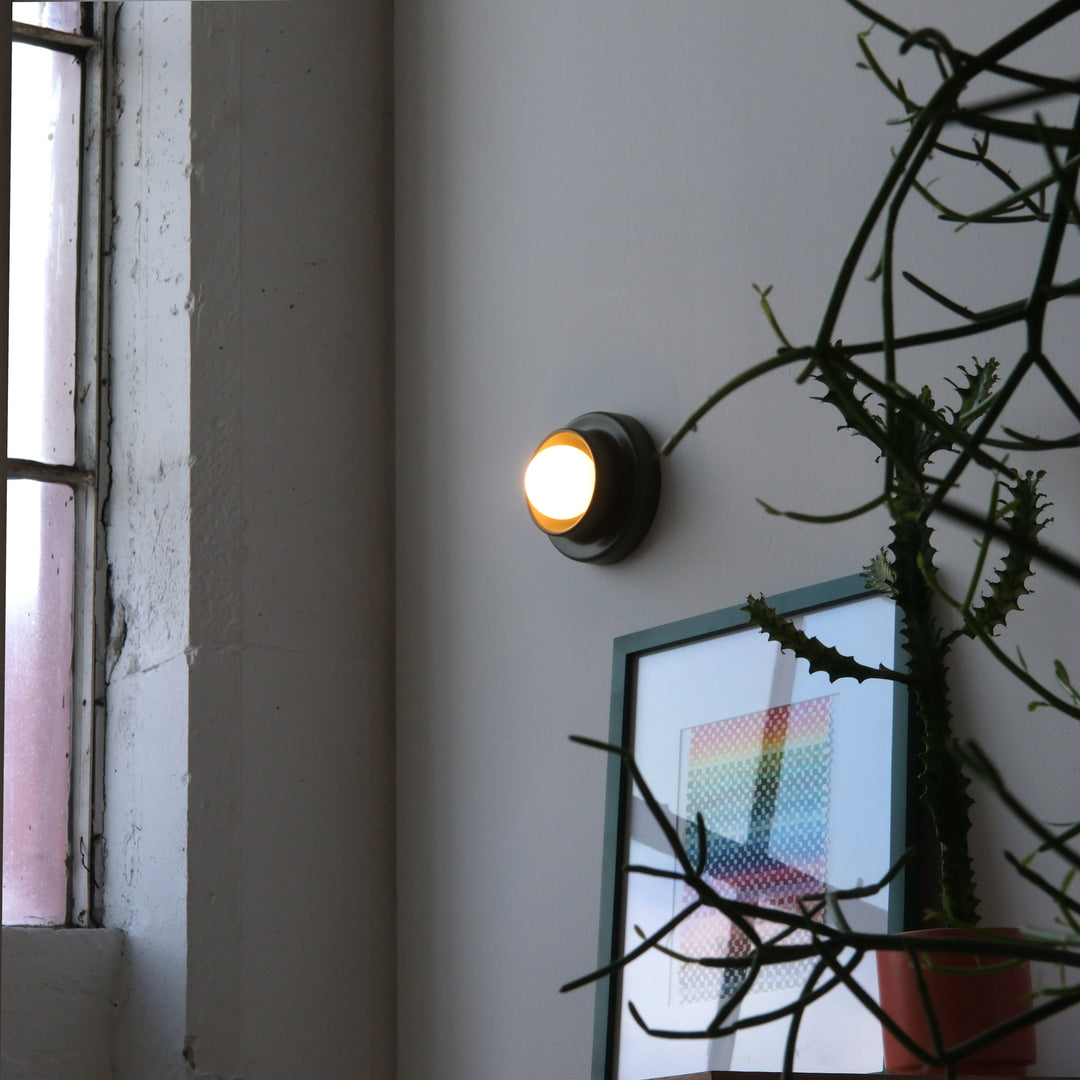 Brass wall sconce casting warm glow beside potted plant and abstract art in minimalist interior