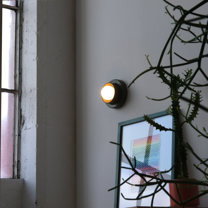 Brass wall sconce casting warm glow beside potted plant and abstract art in minimalist interior