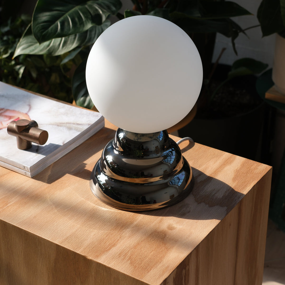 Sleek chrome table lamp with frosted glass globe, styled on light wood side table
