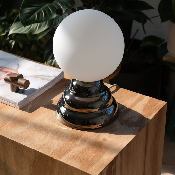 Sleek chrome table lamp with frosted glass globe, styled on light wood side table