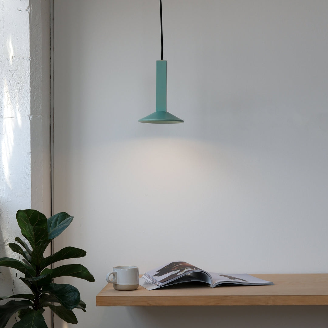 Teal pendant light above wooden shelf with ceramic mug and open magazine, styled with fiddle leaf fig plant