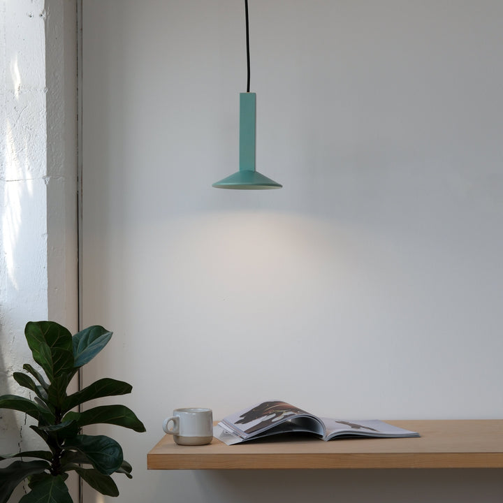 Teal pendant light above wooden shelf with ceramic mug and open magazine, styled with fiddle leaf fig plant