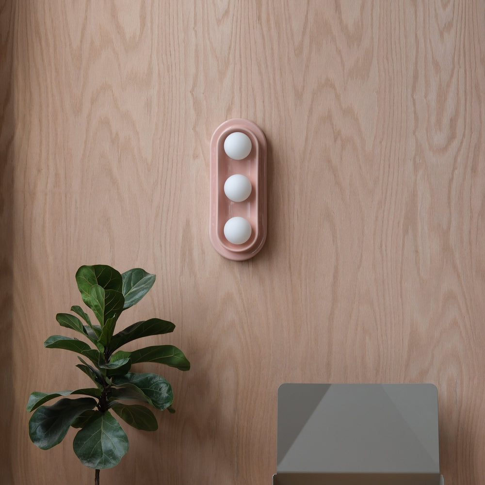 Pink ceramic egg holder with three white eggs, styled on wood with fiddle leaf fig