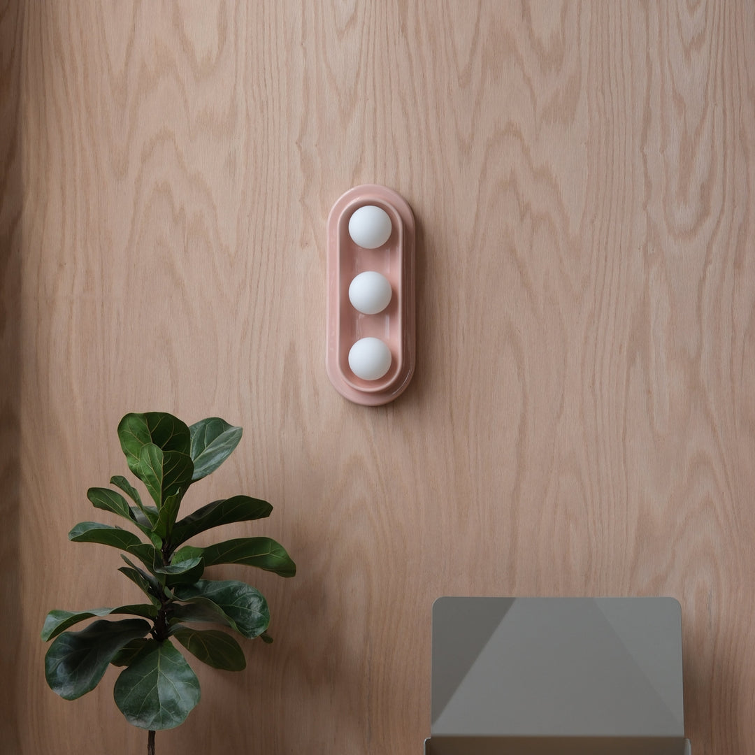 Pink ceramic egg holder with three white eggs, styled on wood with fiddle leaf fig