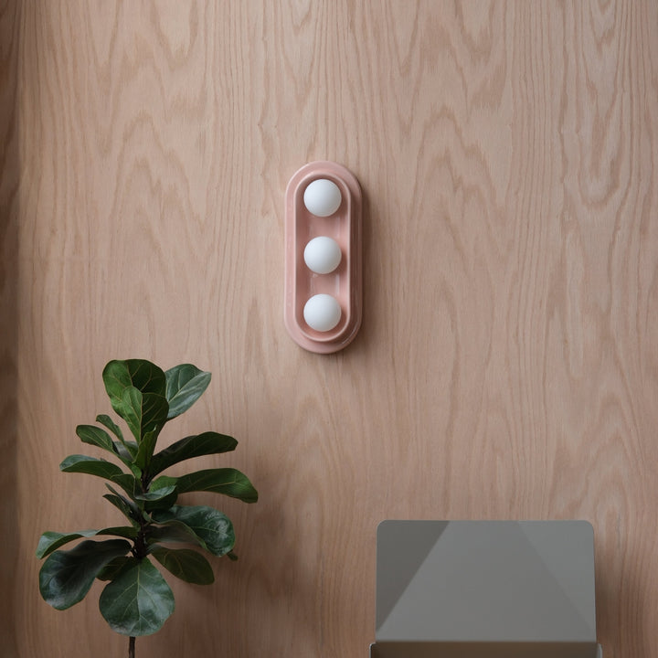 Pink ceramic egg holder with three white eggs, styled on wood with fiddle leaf fig