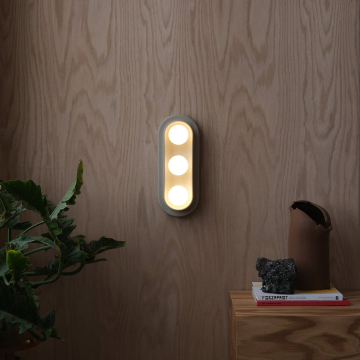 Modern wall sconce with three circular lights, mounted on wood-paneled wall, styled with greenery and decor