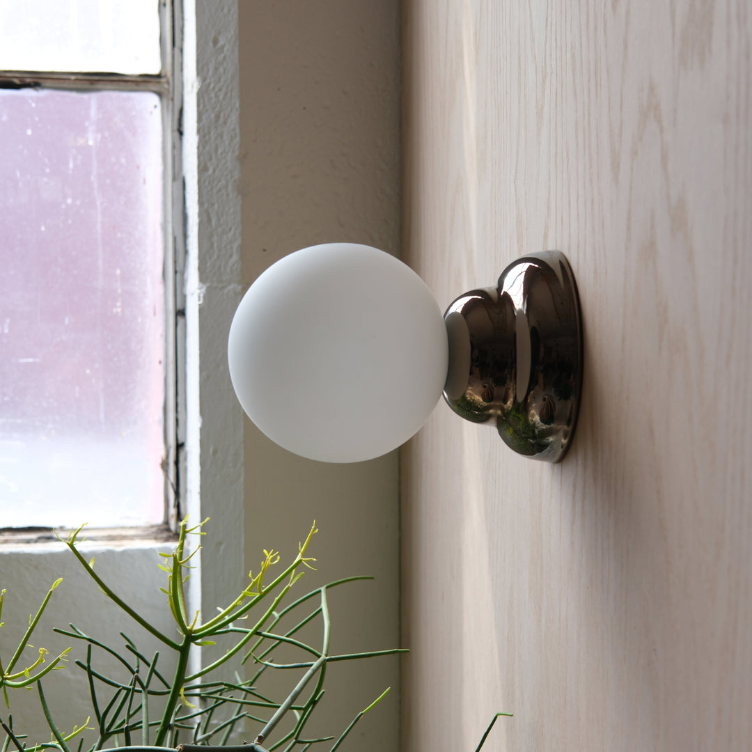 Frosted glass globe sconce with polished chrome heart-shaped backplate, mounted beside a window with greenery