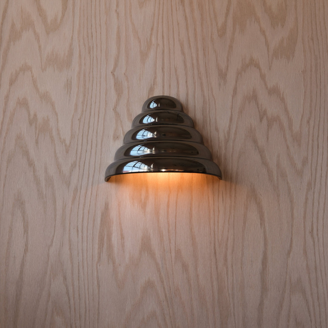 Sleek metallic wall sconce with tiered design, casting warm glow against wood grain backdrop