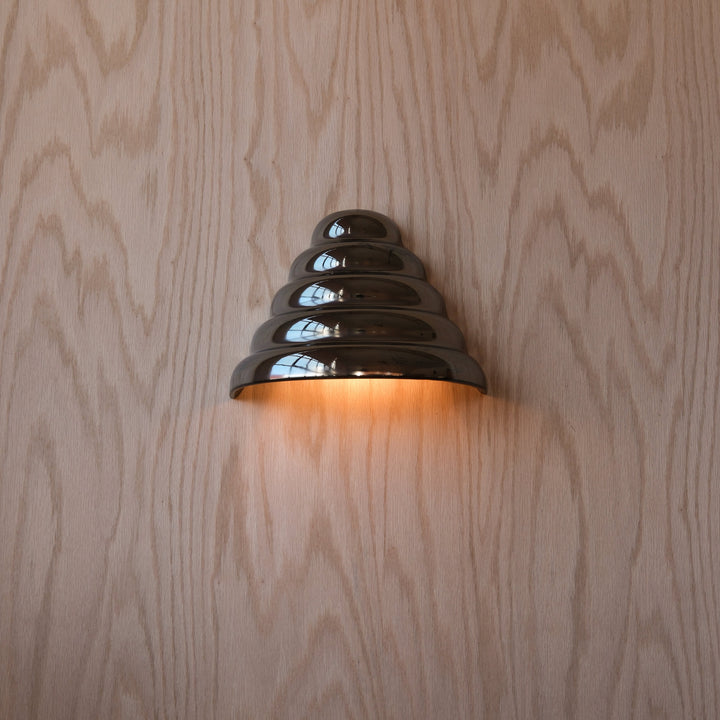 Sleek metallic wall sconce with tiered design, casting warm glow against wood grain backdrop
