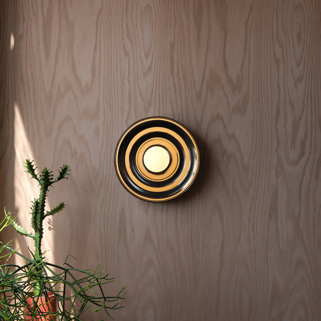 Circular gold and black wall sconce with concentric design, styled against wood paneling