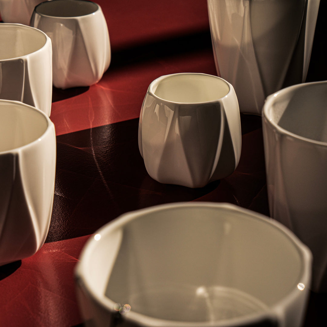 Folio Vessel, Set of 4 — white faceted porcelain vessels grouped on a red and black surface, close lifestyle view