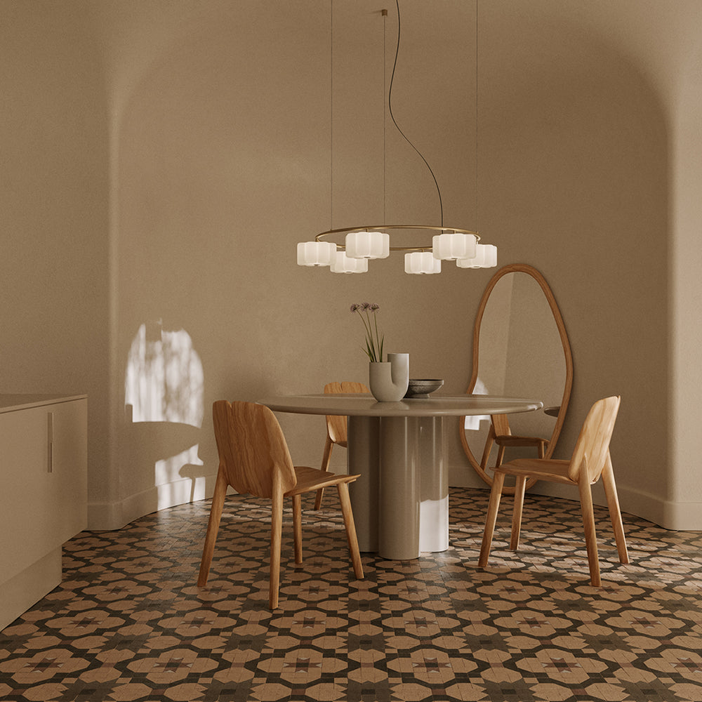 Flow Chandelier in gold, lit over a round dining table with wooden chairs on a patterned tile floor