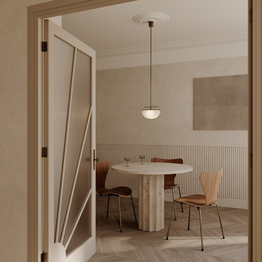 Gina Pendant over a round travertine table with wooden chairs, seen through an open doorway