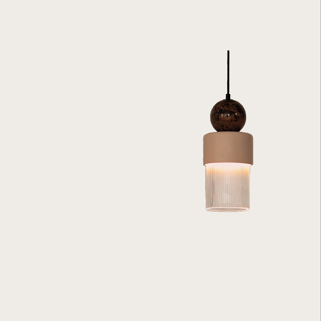 A modern pendant light fixture with a dark brown spherical top, a beige cylindrical shade, and a ribbed clear glass lower shade, suspended against a solid off-white background.