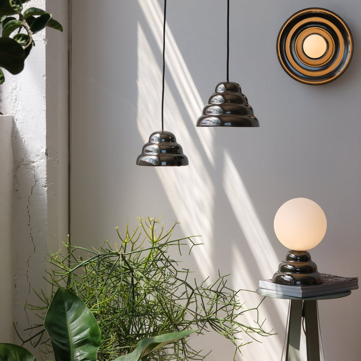 Sleek tiered pendant lights with glossy finish, paired with a spherical table lamp and lush greenery.