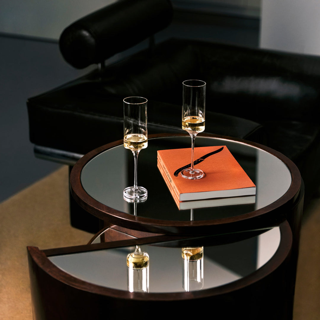 Hew Champagne Flute, Set of 2 — two filled flutes on a mirrored side table with a book