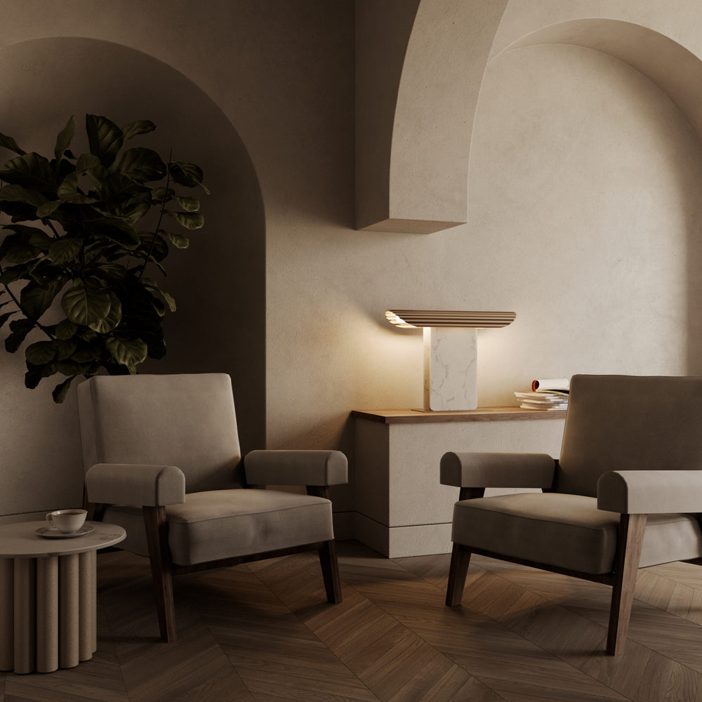 Lit white marble and gold table lamp on a console between two armchairs under a plaster arch