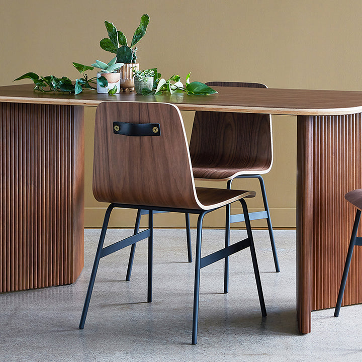 Walnut dining chair with black metal legs and leather handle, styled with greenery