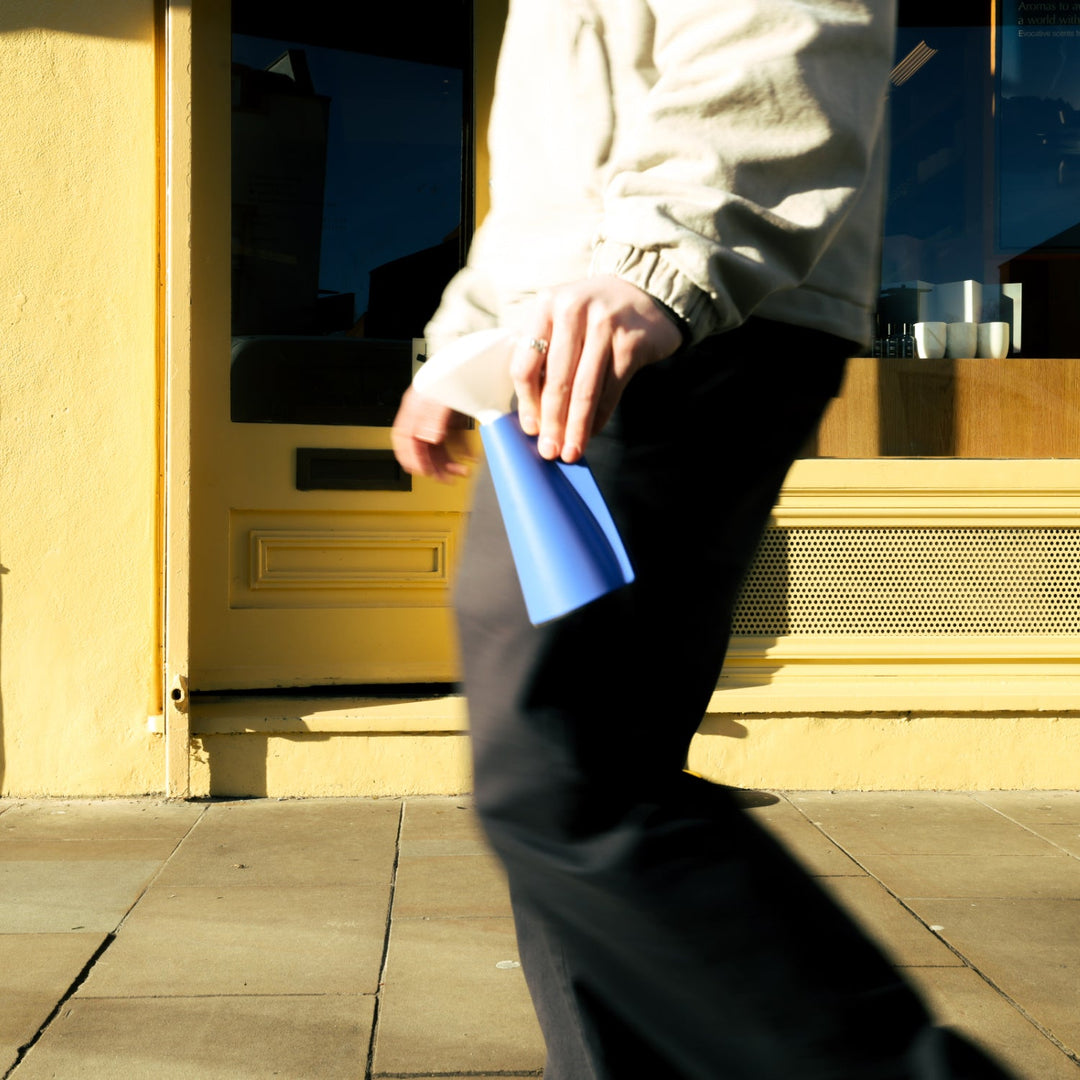 Elegant blue ceramic vase held against sunlit yellow doorway, minimalist home decor