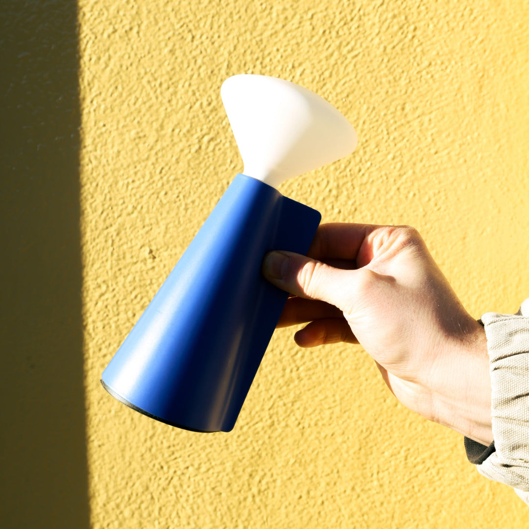 Blue ceramic table lamp with white shade, held against yellow textured wall