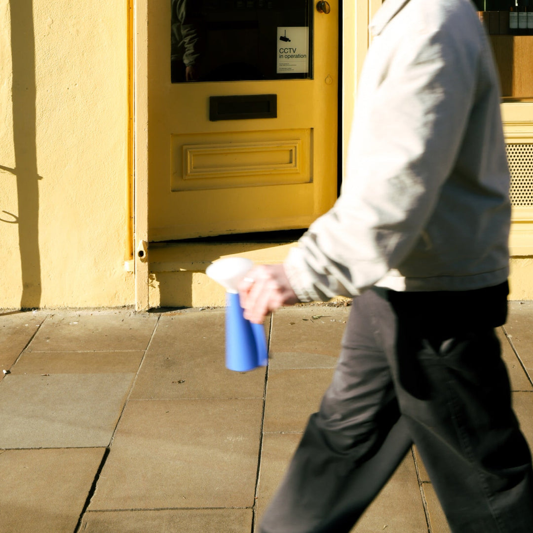 Person holding blue spray bottle near yellow door with CCTV sign