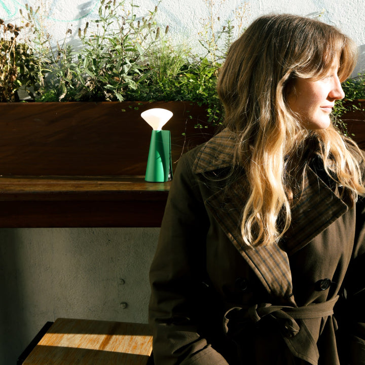 Green ceramic table lamp with white shade, styled beside a woman in a trench coat