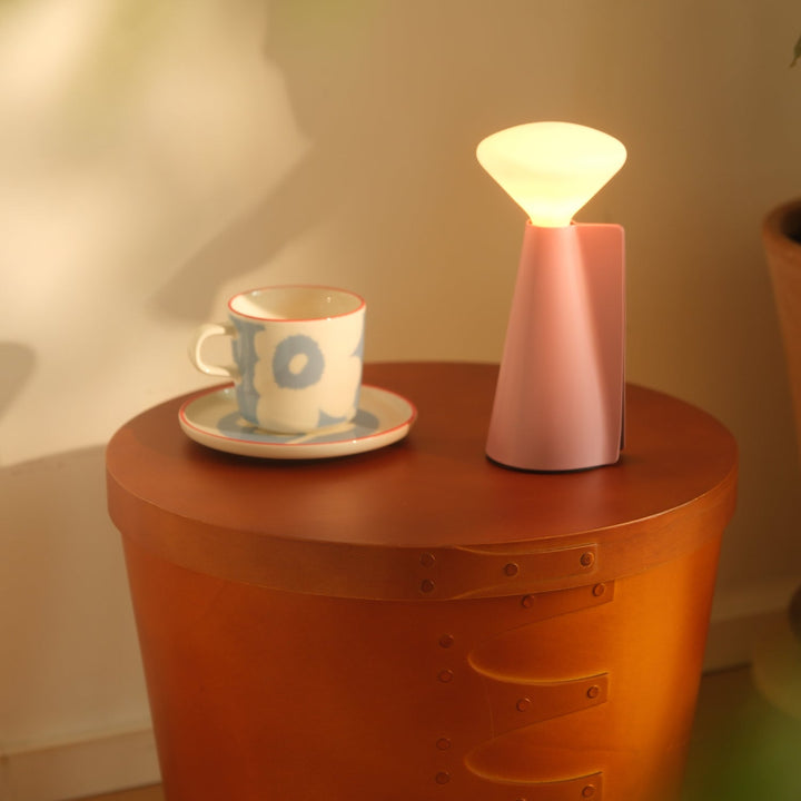 Pink ceramic table lamp with warm glow beside floral teacup on terracotta side table