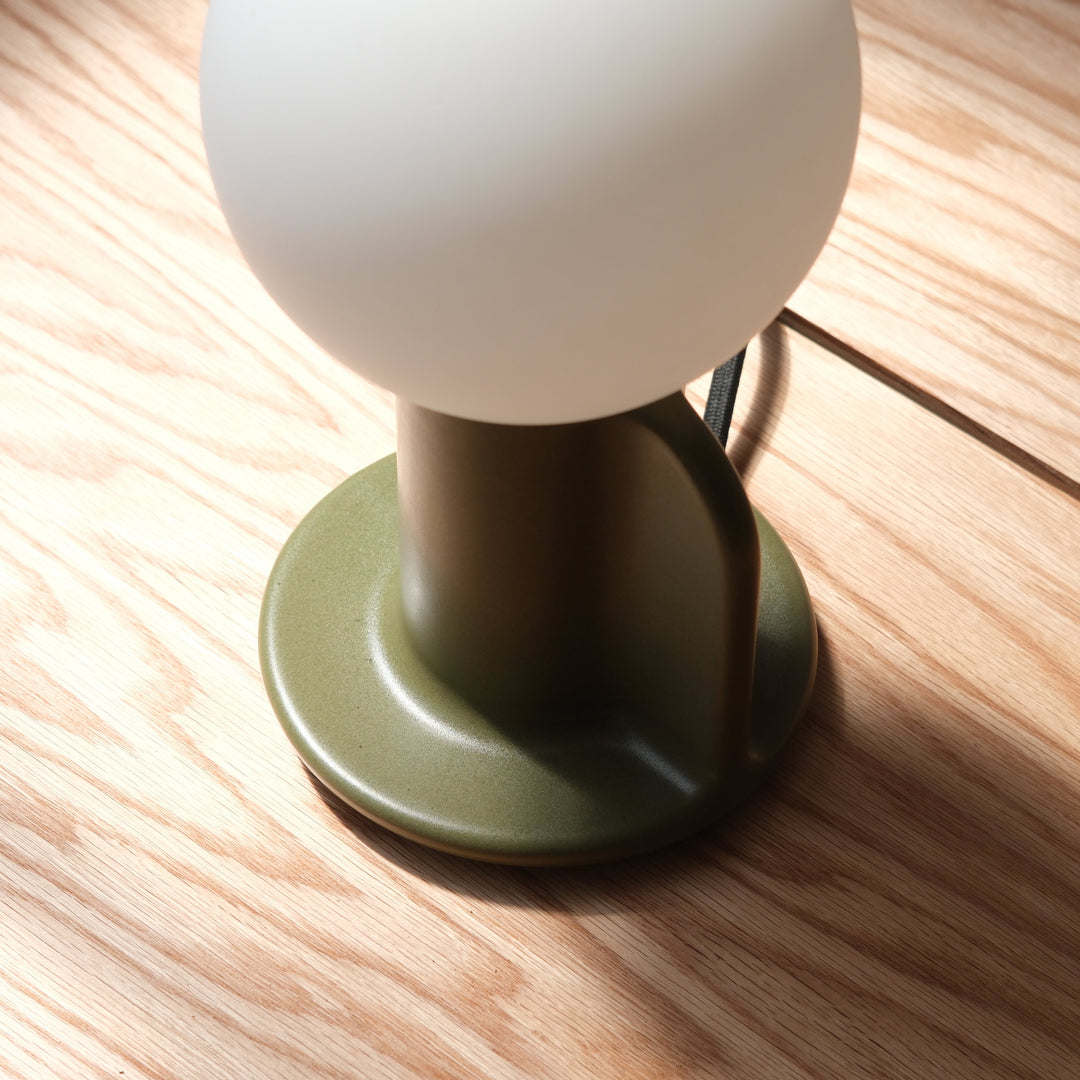 Sleek table lamp with matte olive base and frosted globe shade on wood surface