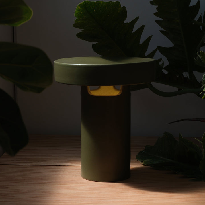 Olive green ceramic stool with golden accent, nestled among lush foliage