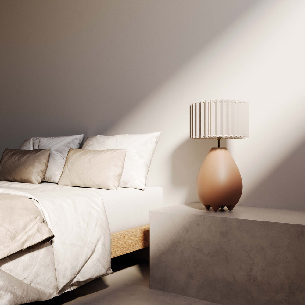 Terracotta ceramic lamp on a concrete nightstand next to a bed with linen pillows in soft light