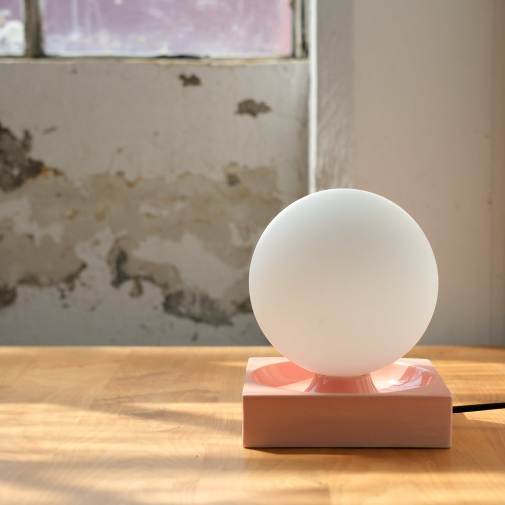 Frosted glass globe lamp on blush ceramic base, modern minimalist design