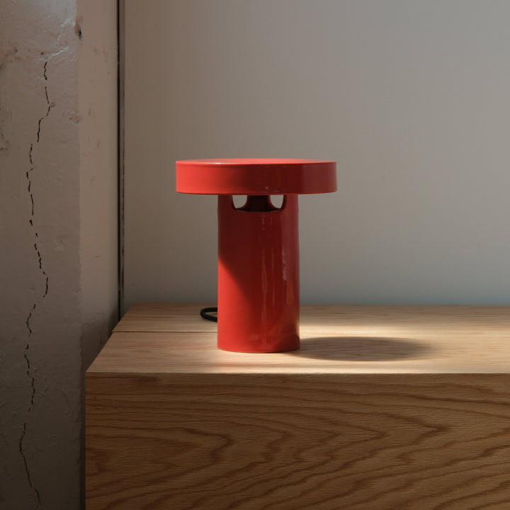 Sleek red ceramic table lamp with minimalist design, casting soft shadows on wood surface