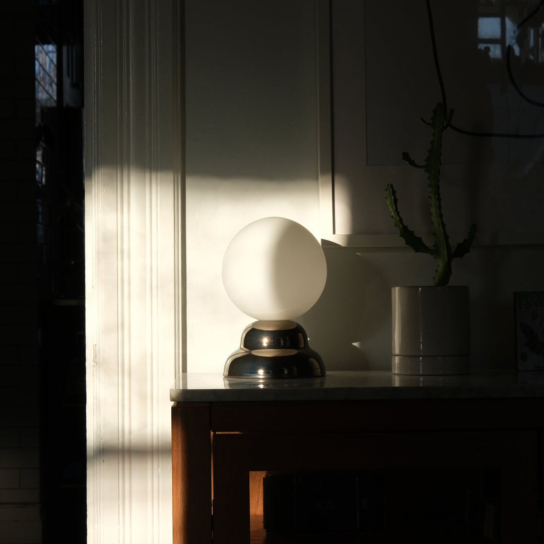 Sleek glass globe lamp with polished metal base, styled on marble console beside potted cactus