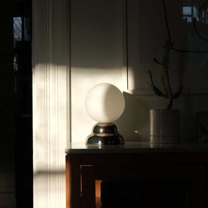 Sleek glass globe lamp with polished metal base, styled on marble console beside potted cactus