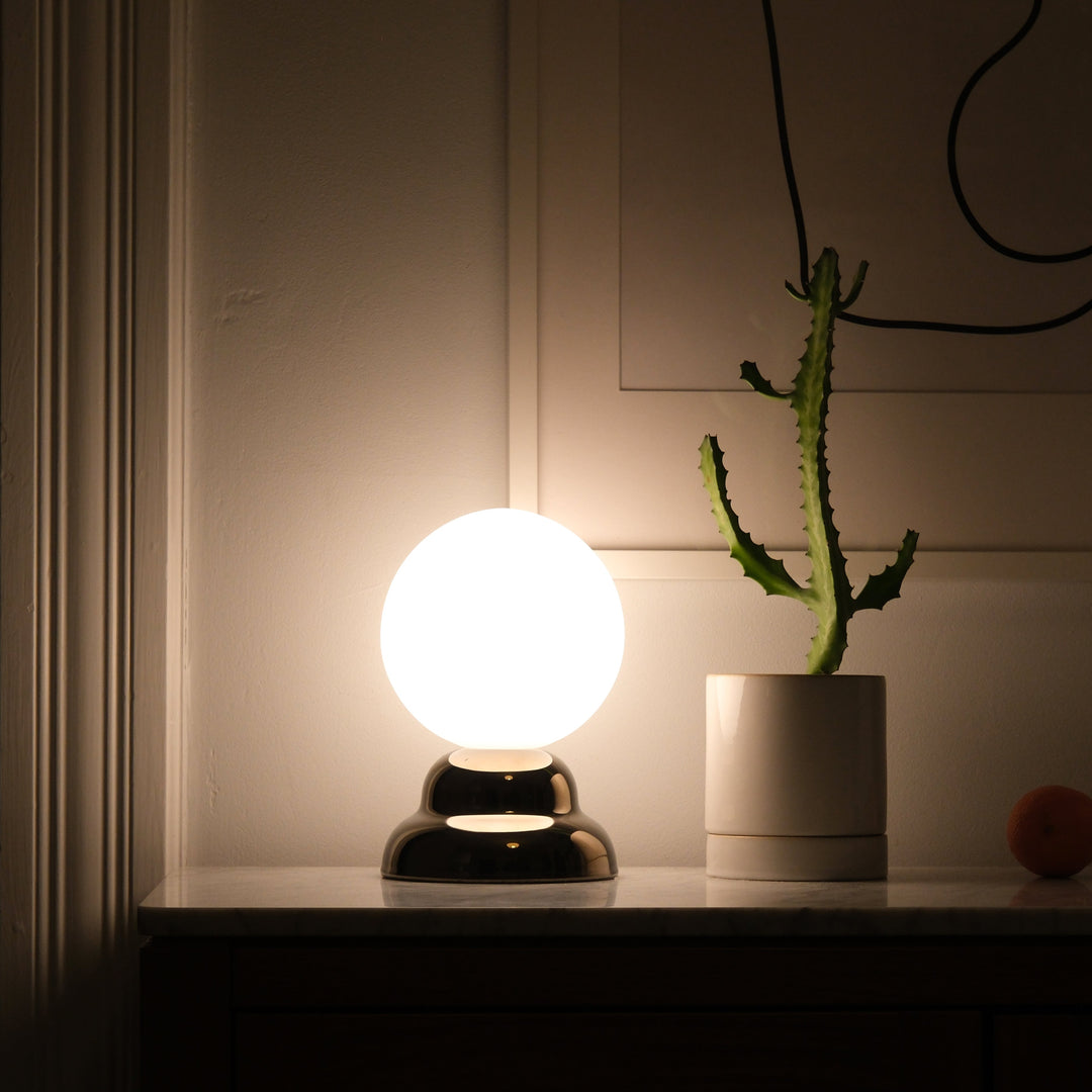 Globe table lamp with glossy black base, glowing softly beside potted cactus on marble surface