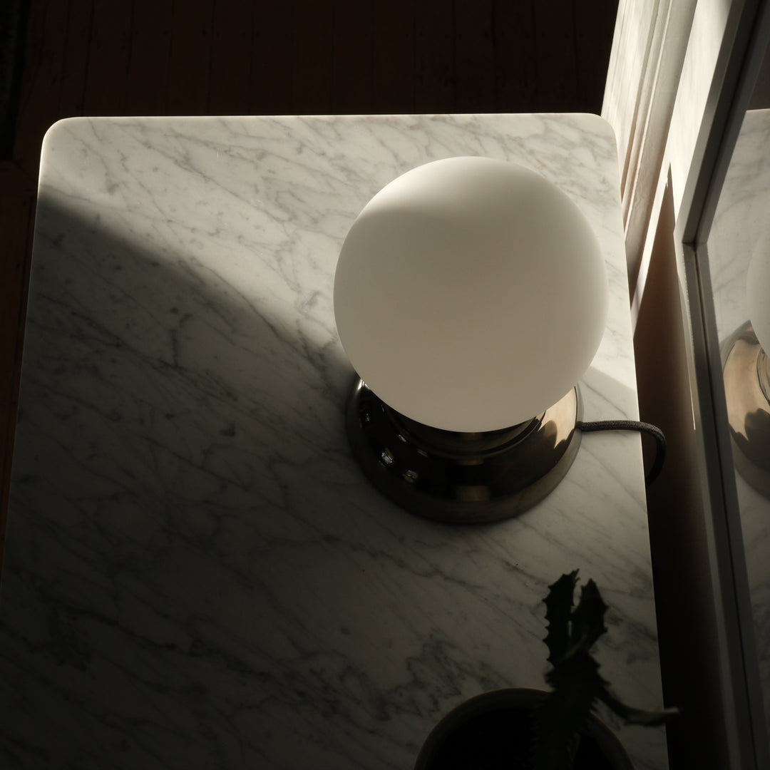 Sleek frosted glass table lamp with polished brass base on marble surface