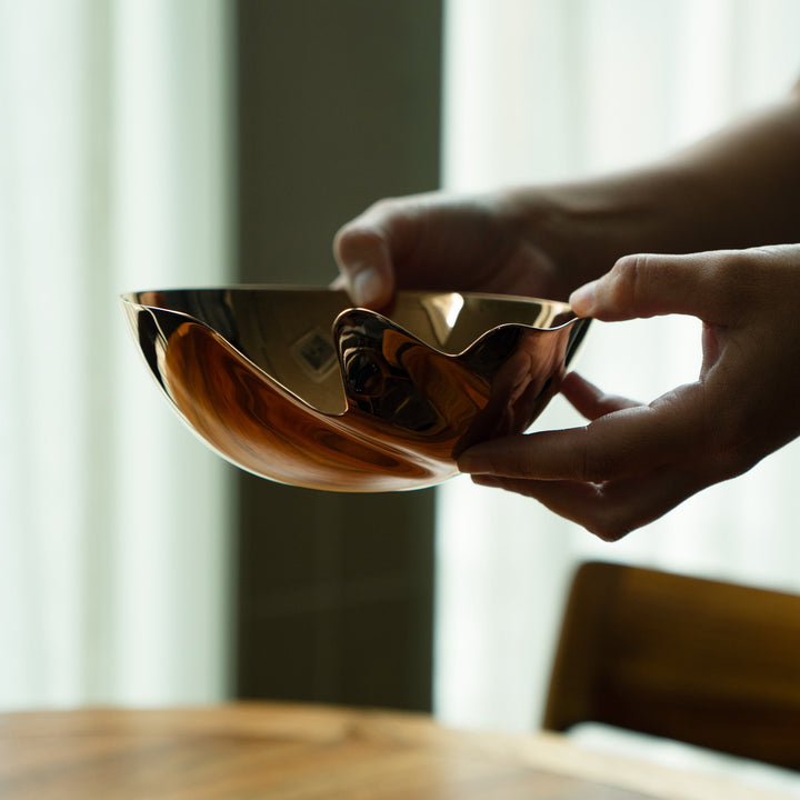 Serenity Bowl — rose gold bowl held in two hands above a wooden dining table
