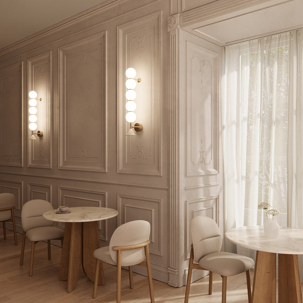 Two Soko Wall Lamps lit on panelled walls of a cafe with marble tables and upholstered chairs