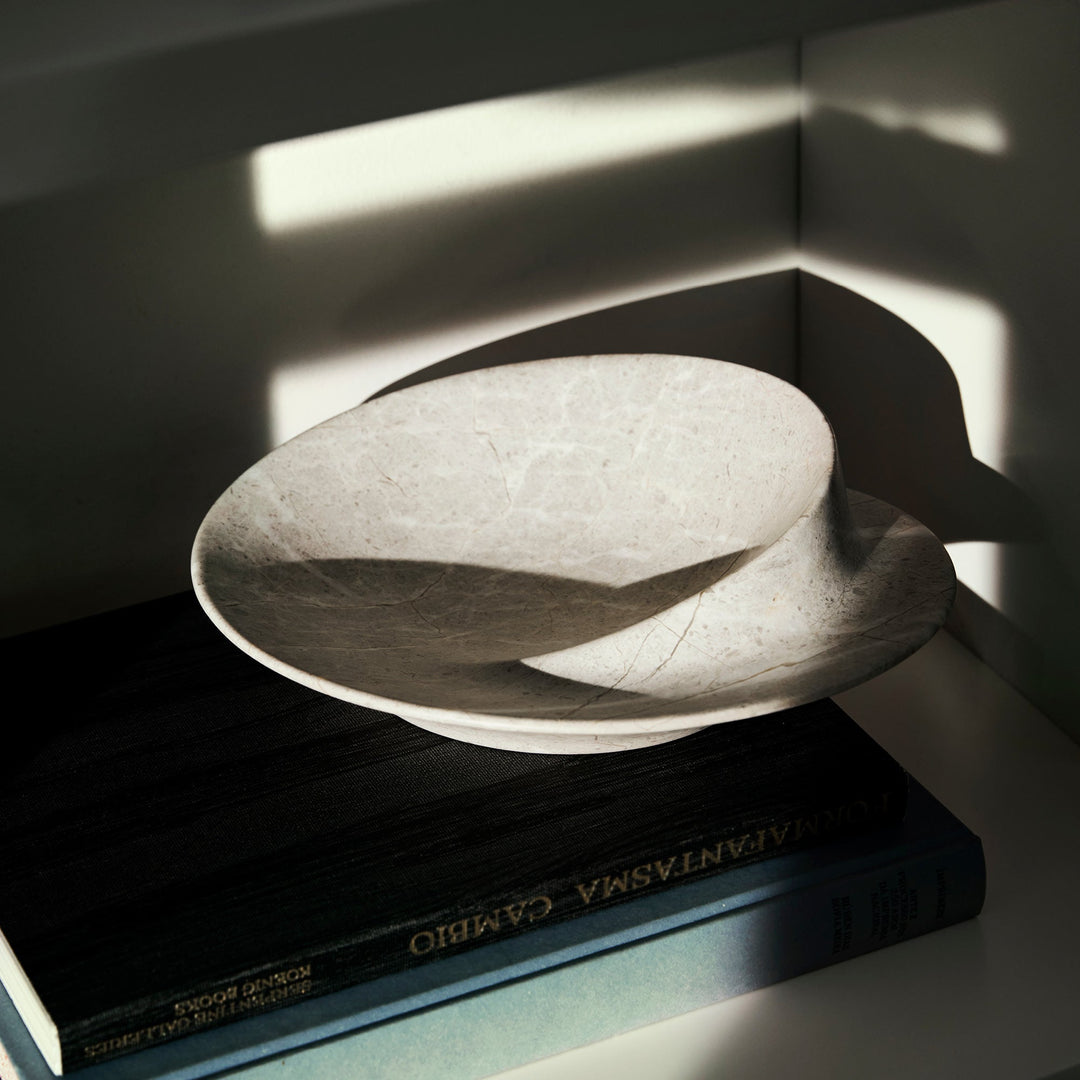 Swirl Bowl — small Grey Marble bowl on a dark book in raking sunlight