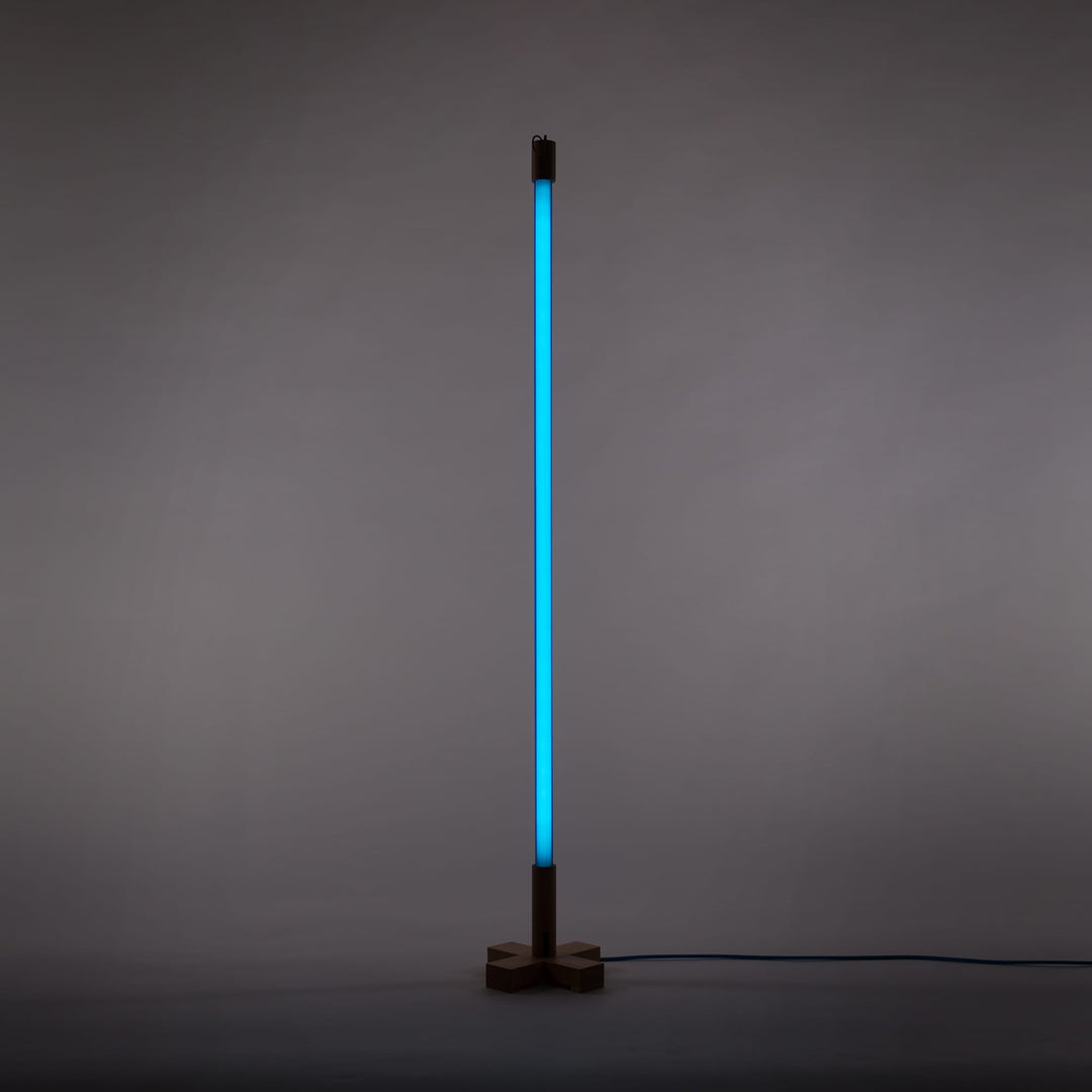 Seletti Linea LED Blue, blue tube lit upright on its wooden stand against a gray wall