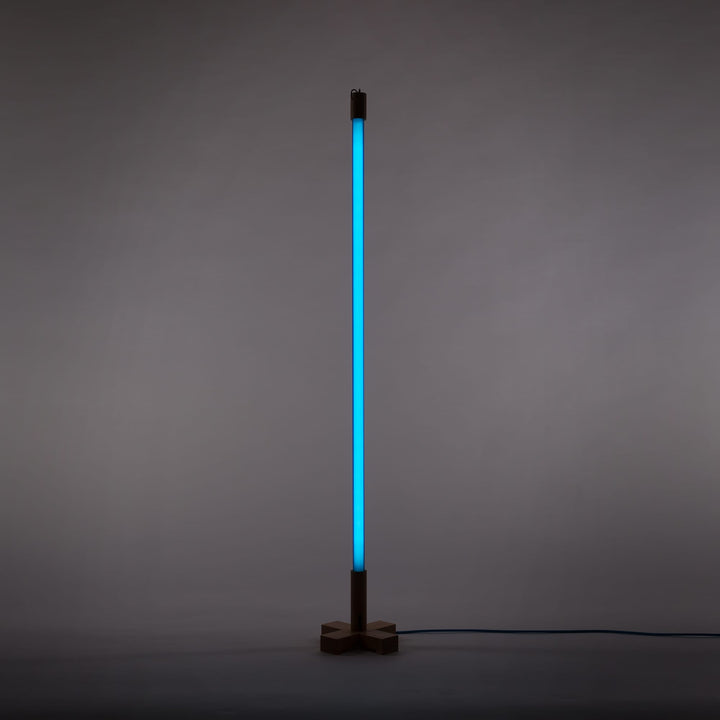 Seletti Linea LED Blue, blue tube lit upright on its wooden stand against a gray wall