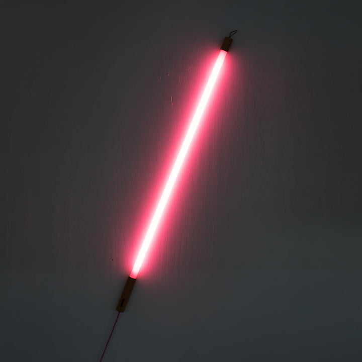 Seletti Linea LED Pink, pink tube glowing bright on the diagonal against a dark wall